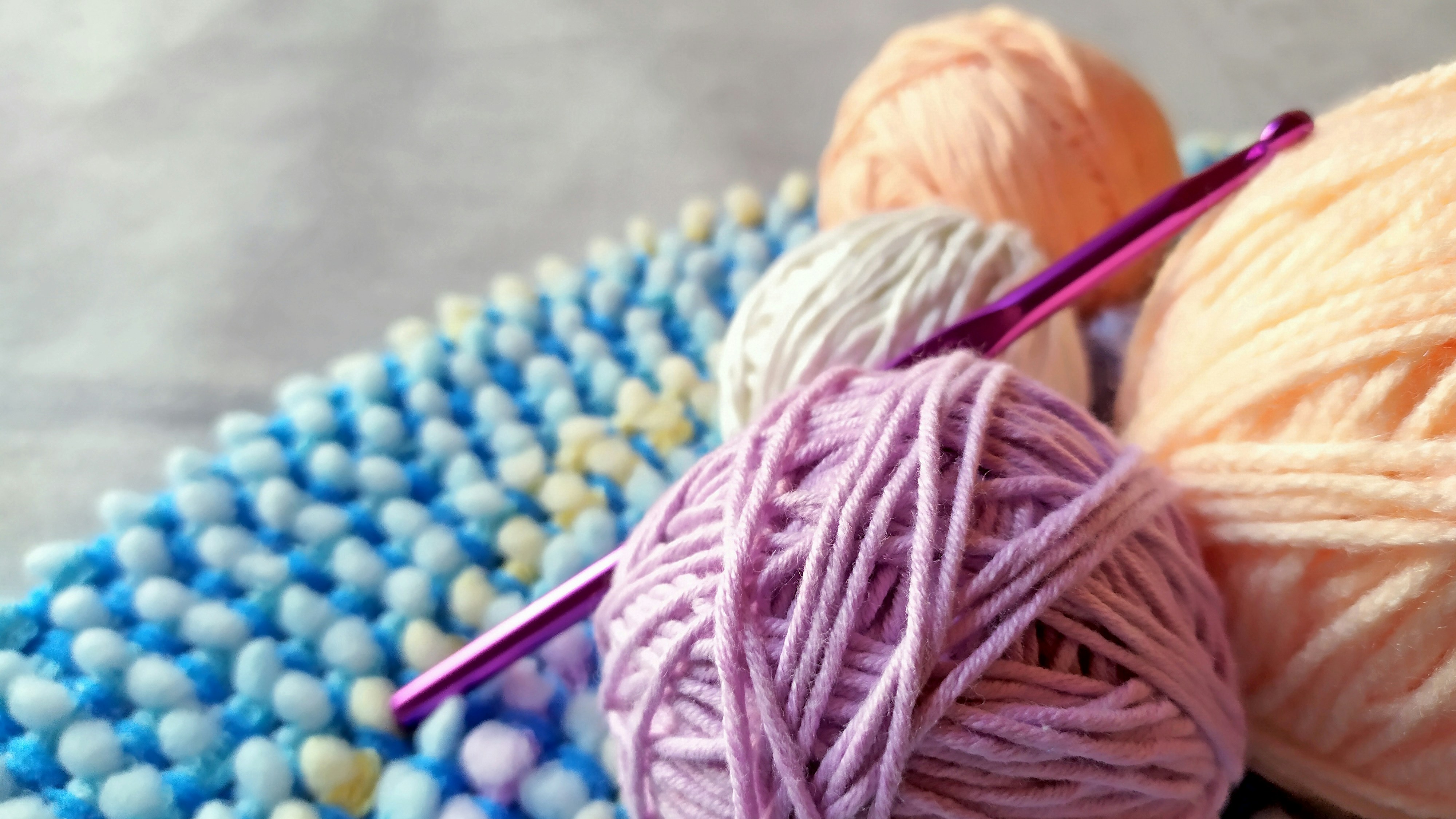 Bunte Wolle in Pastelltönen, DIY-Handarbeit mit gehäkelter Struktur, Akzente in Blau und Weiß.