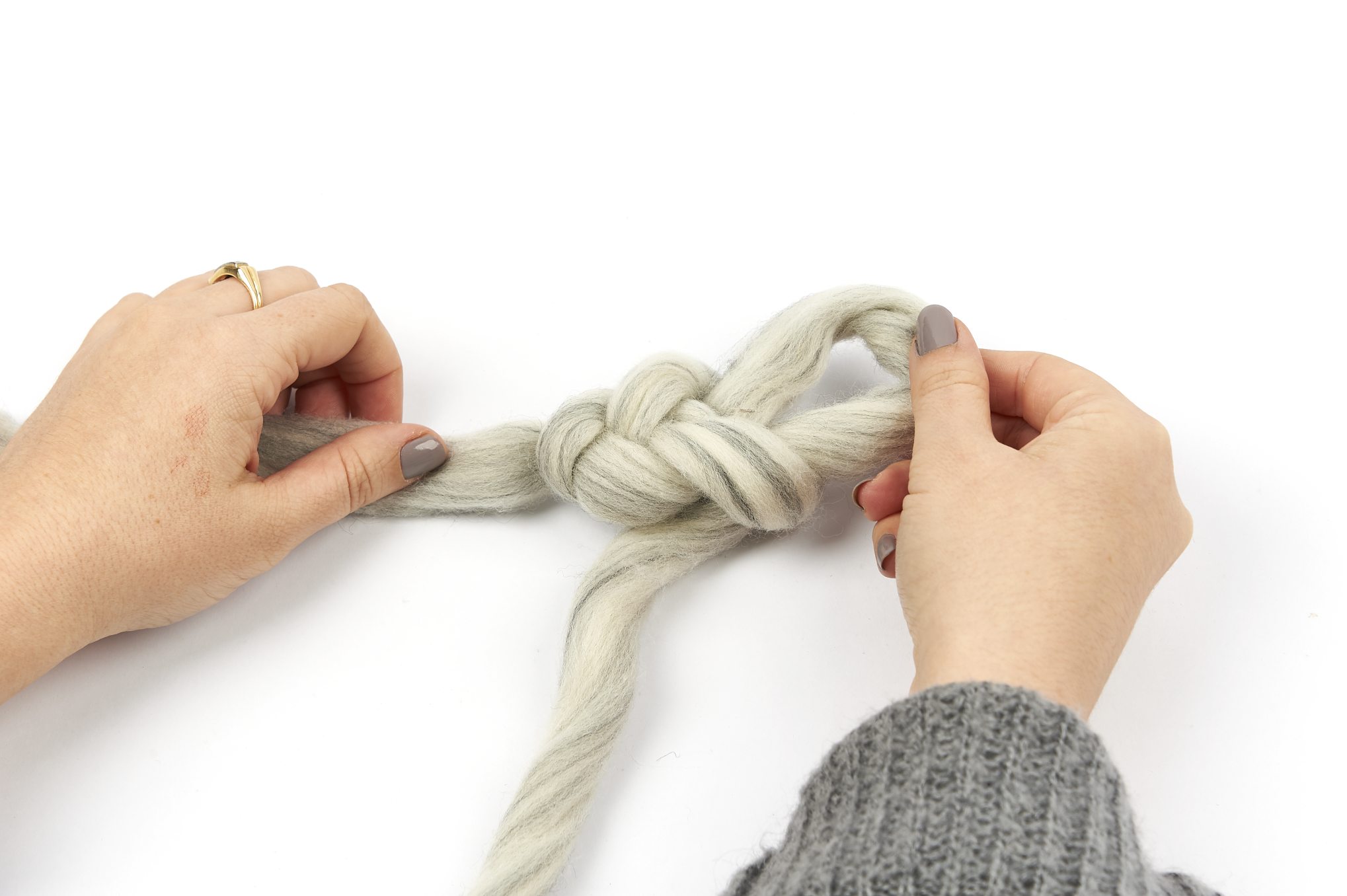 Graue Wolle mit handgemachtem Knoten, begleitet von gestricktem Pulli. Modern und DIY-inspiriert.