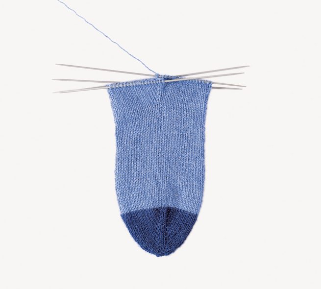 Handgestrickter Sockenanfang in Blau mit dunkler Spitze. Modisch, diy, detailreich, handgearbeitet.