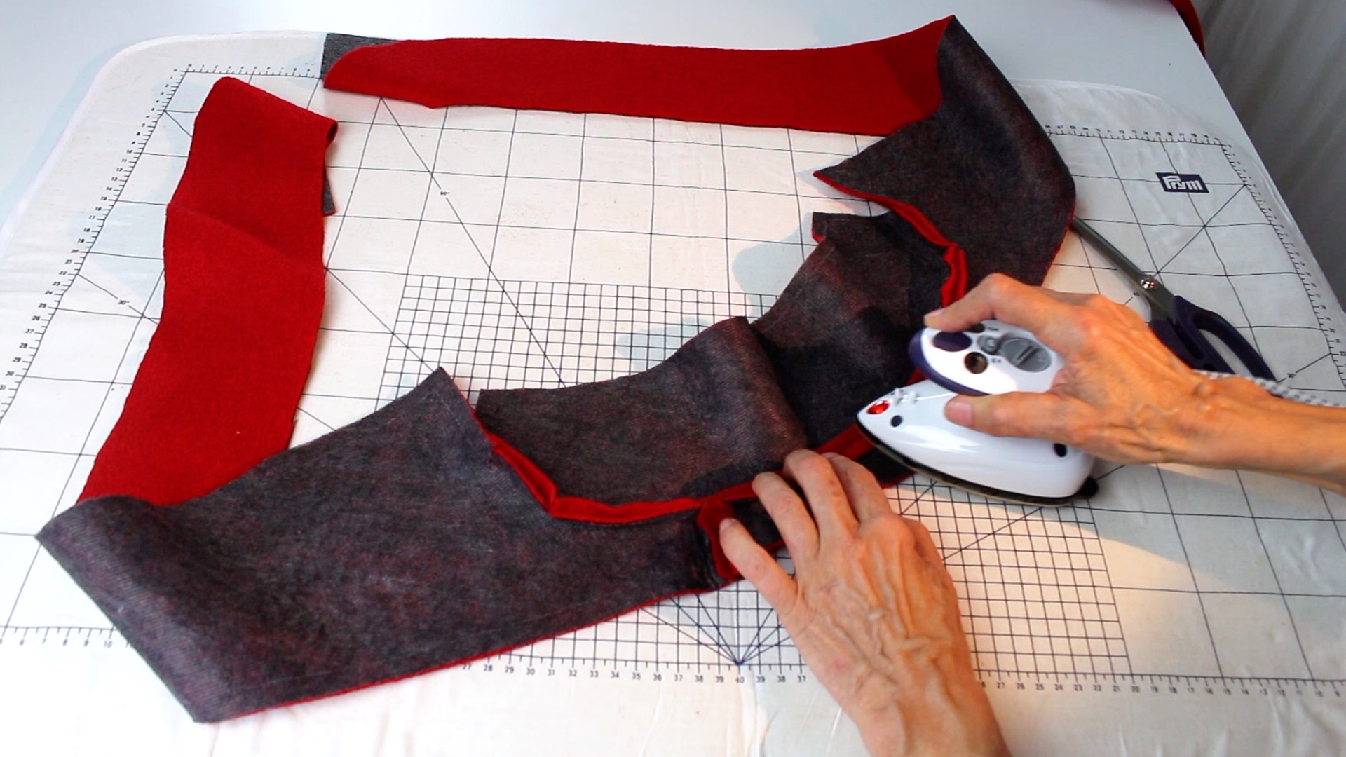 Modisches DIY-Projekt: Rote und graue Stoffstreifen werden präzise mit einem Mini-Bügeleisen in Form gebracht.