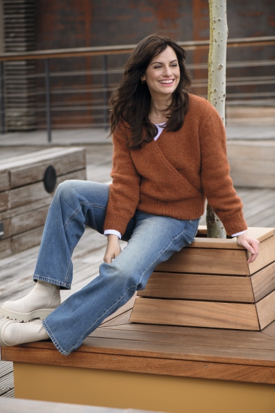 Rostfarbener Strickpulli, Wickelschnitt; blaue, ausgestellte Jeans; cremefarbene Stiefeletten. Modisch, bequem.