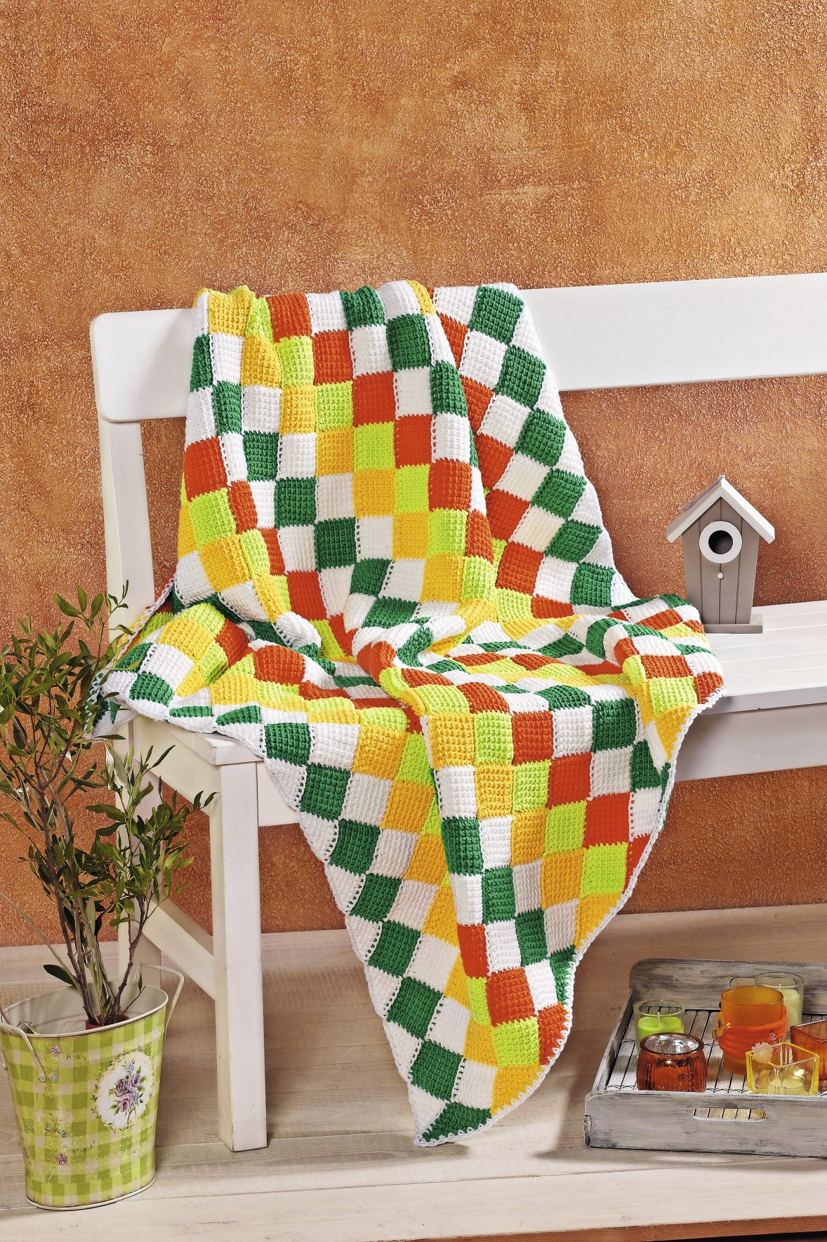 Handgemachte Decke im Patchwork-Stil. Farbige Quadrate in Grün, Gelb, Weiß und Orange. Modisch und DIY.