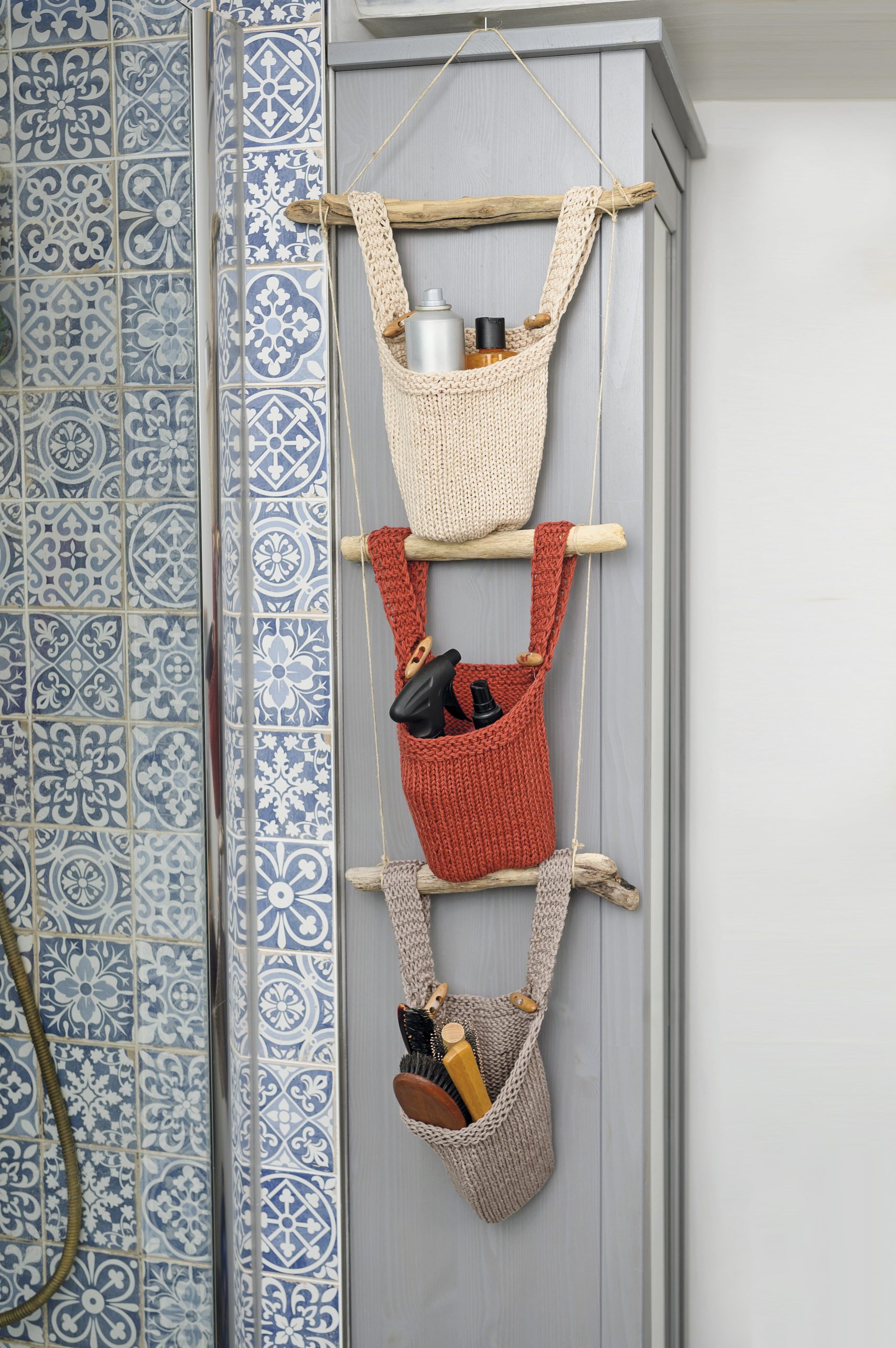 DIY Hängeorganizer mit drei gestrickten Taschen in Beige, Rot, Braun. Natürliche Holzstäbe als Träger.