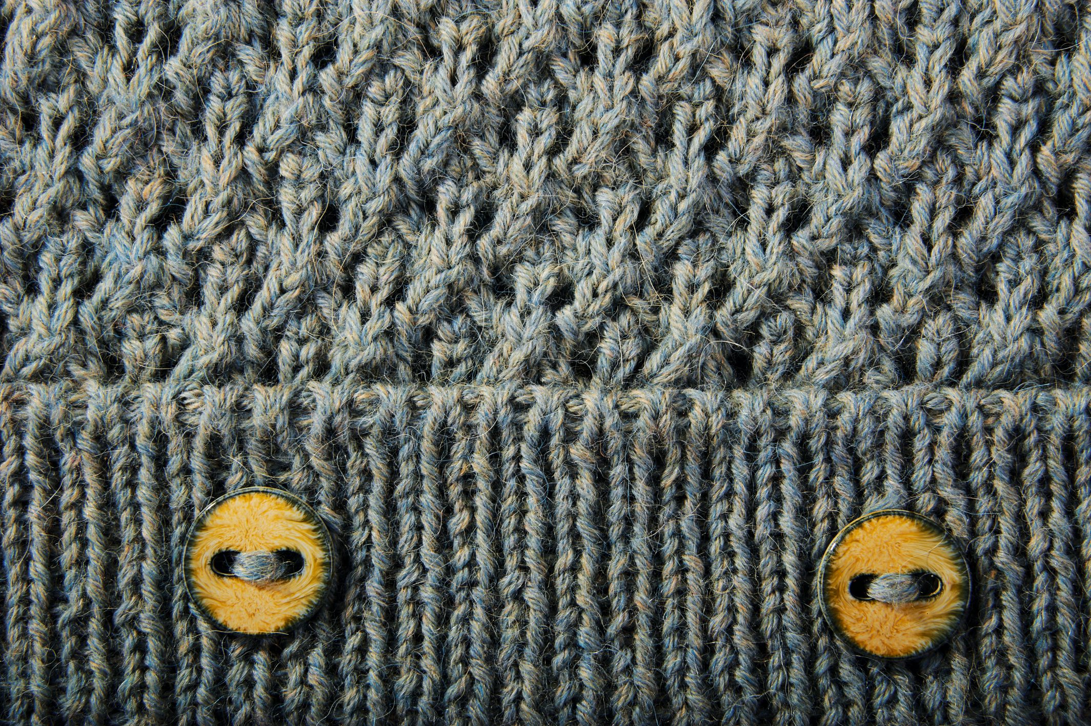 Gestricktes Muster in Grautönen, handgemacht. Gelbe Knöpfe als Akzent, modisch und detailliert.