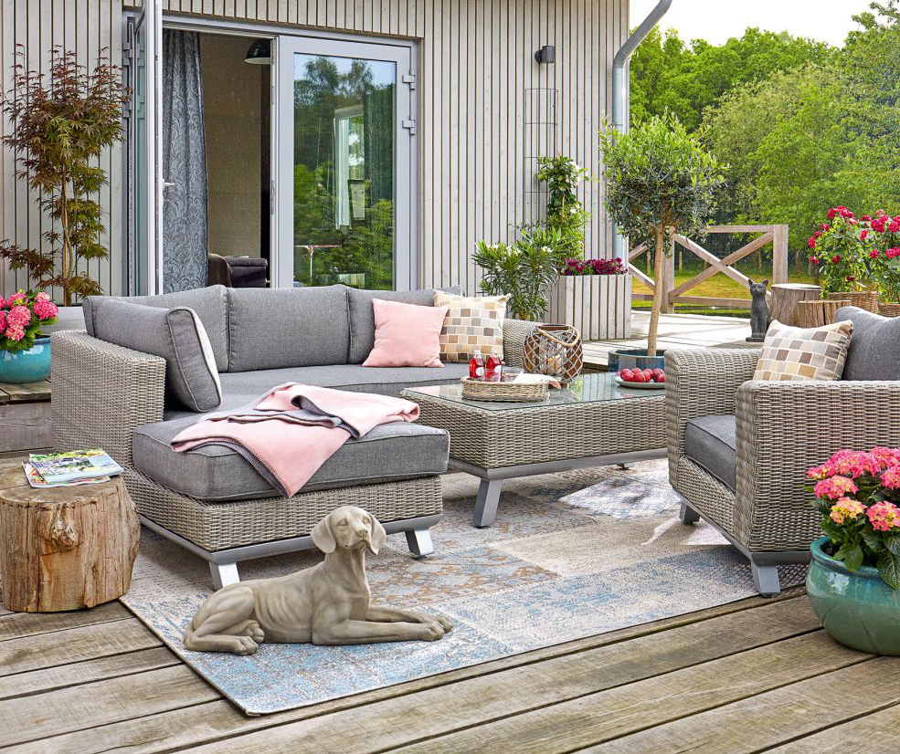 Graue Rattan-Möbel mit pastellrosa Kissen, handgewebt. Schlichte, zeitgenössische Eleganz im Outdoor-Stil.