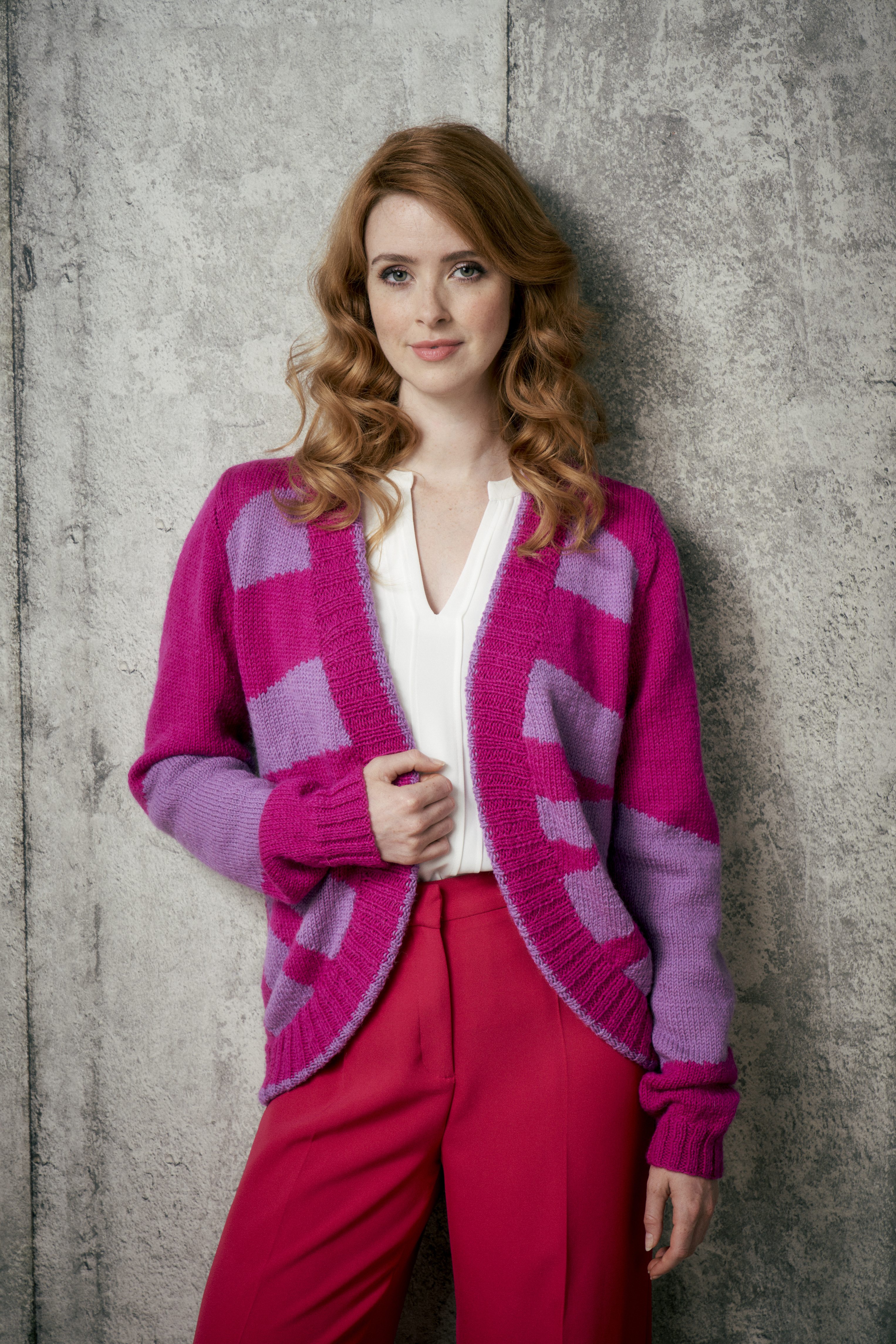 Fuchsia-lila Cardigan mit geometrischem Muster, kombiniert mit weißer Bluse und roten Hose. Trendy und handgemacht.