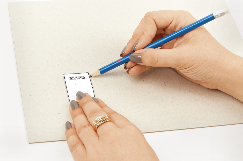 Person zeichnet mit blauem Stift auf Papier. Dezente Kleidung, grauer Nagellack, elegante Ringe.