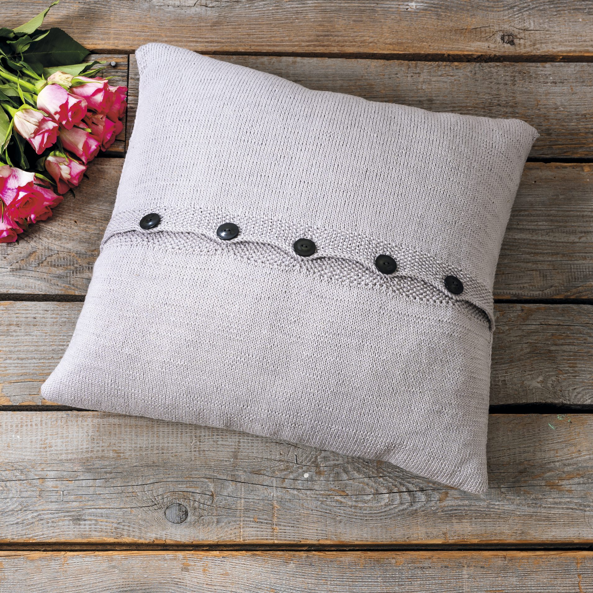 Handgemachtes weiches Kissen mit grauem Strickmuster, schwarzen Knöpfen, elegant und modern.