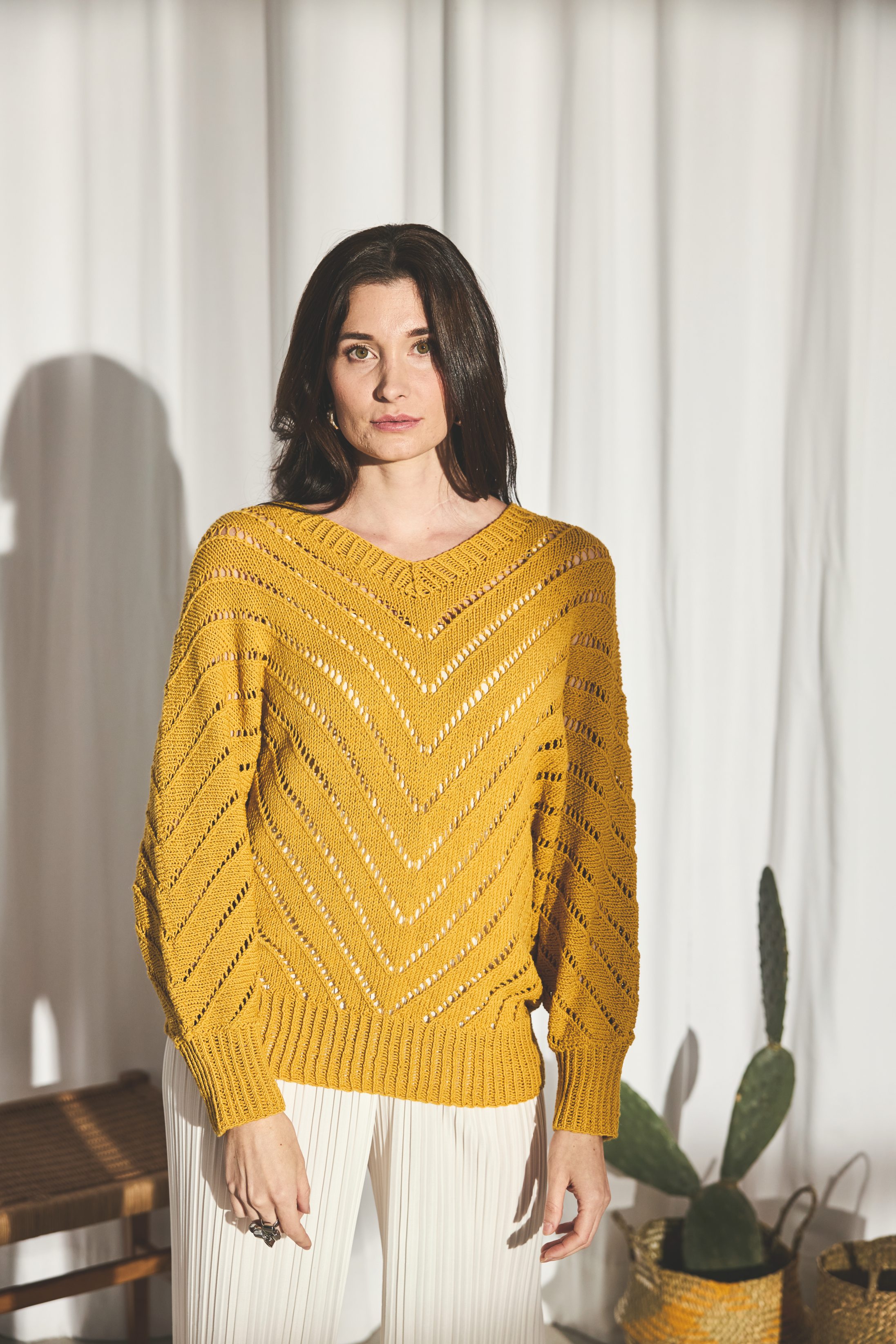 Senfgelber V-Pullover mit Chevron-Muster; lässig, handgemacht, DIY-Strickstil. Kombiniert mit weißen Hosen.