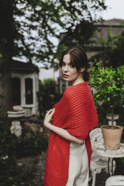 Roter handgemachter Strickschal, texturiertes Muster, lässig umgeworfen über schlichte, helle Kleidung.