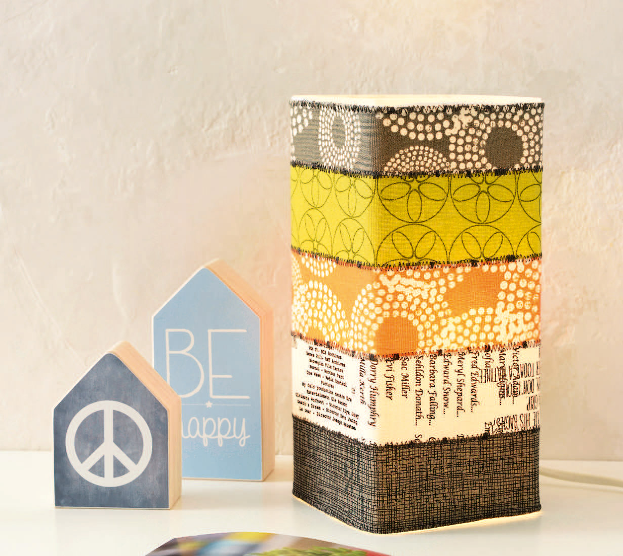 Bunte, handgemachte Lampenhülle mit geometrischen und schriftgemusterten Stoffstreifen. Kreatives DIY-Design.