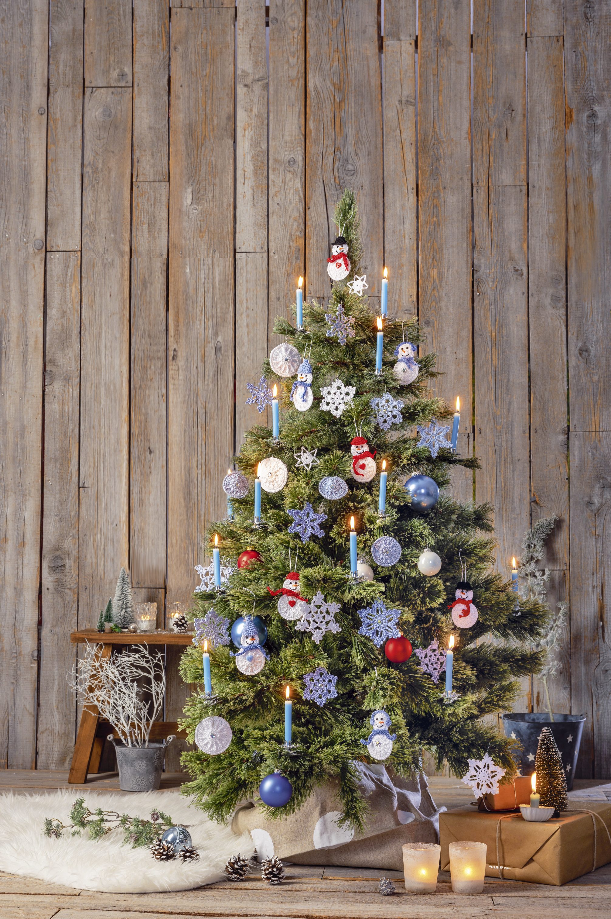 Weihnachtsbaum mit handgemachten, blauen und roten Ornamenten. Modische Schneeflockenmuster, stilvoll geschmückt.