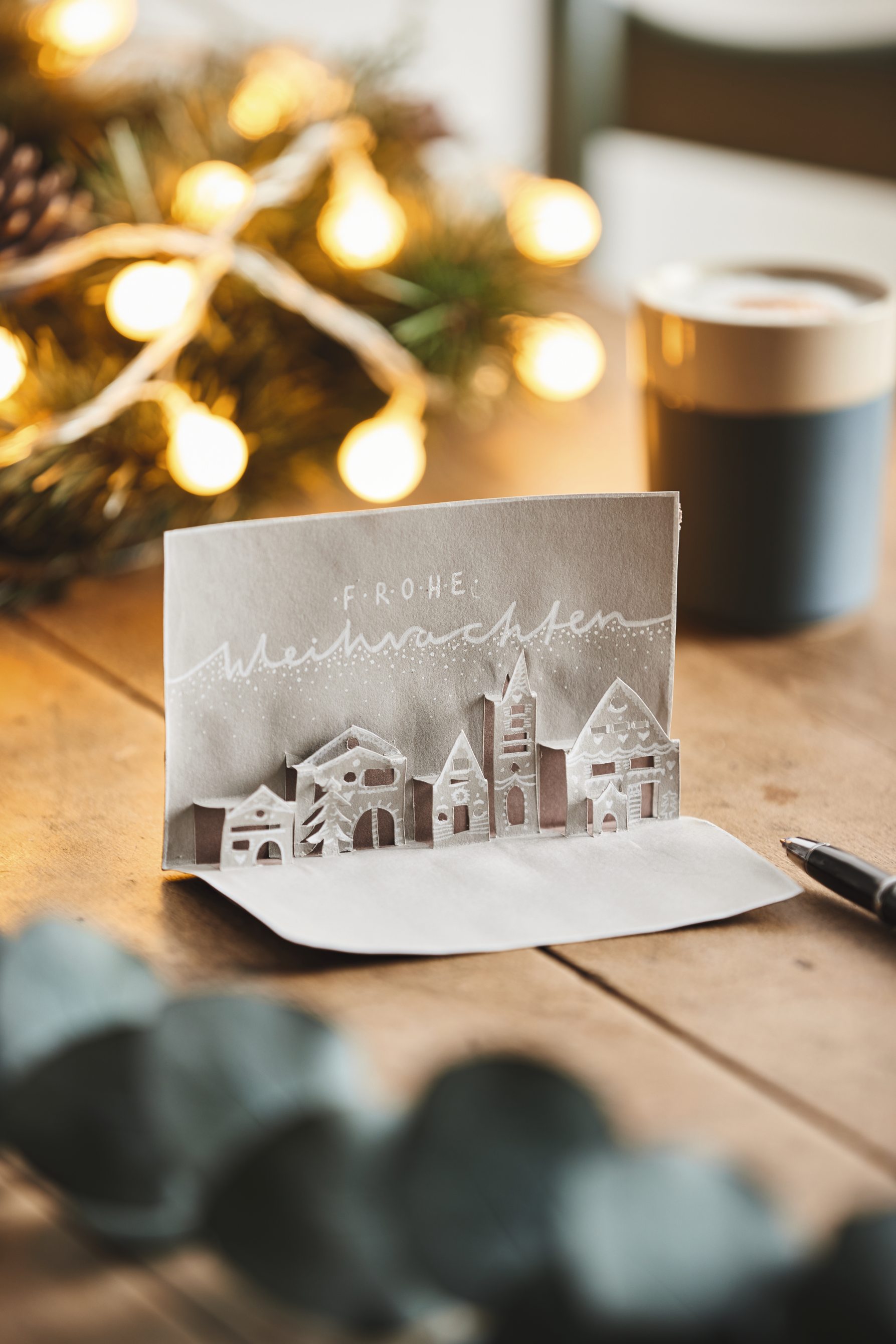 Graue, DIY-Weihnachtskarte mit filigranen, ausgeschnittenen Häusern; minimalistisch, elegant, handgefertigt.