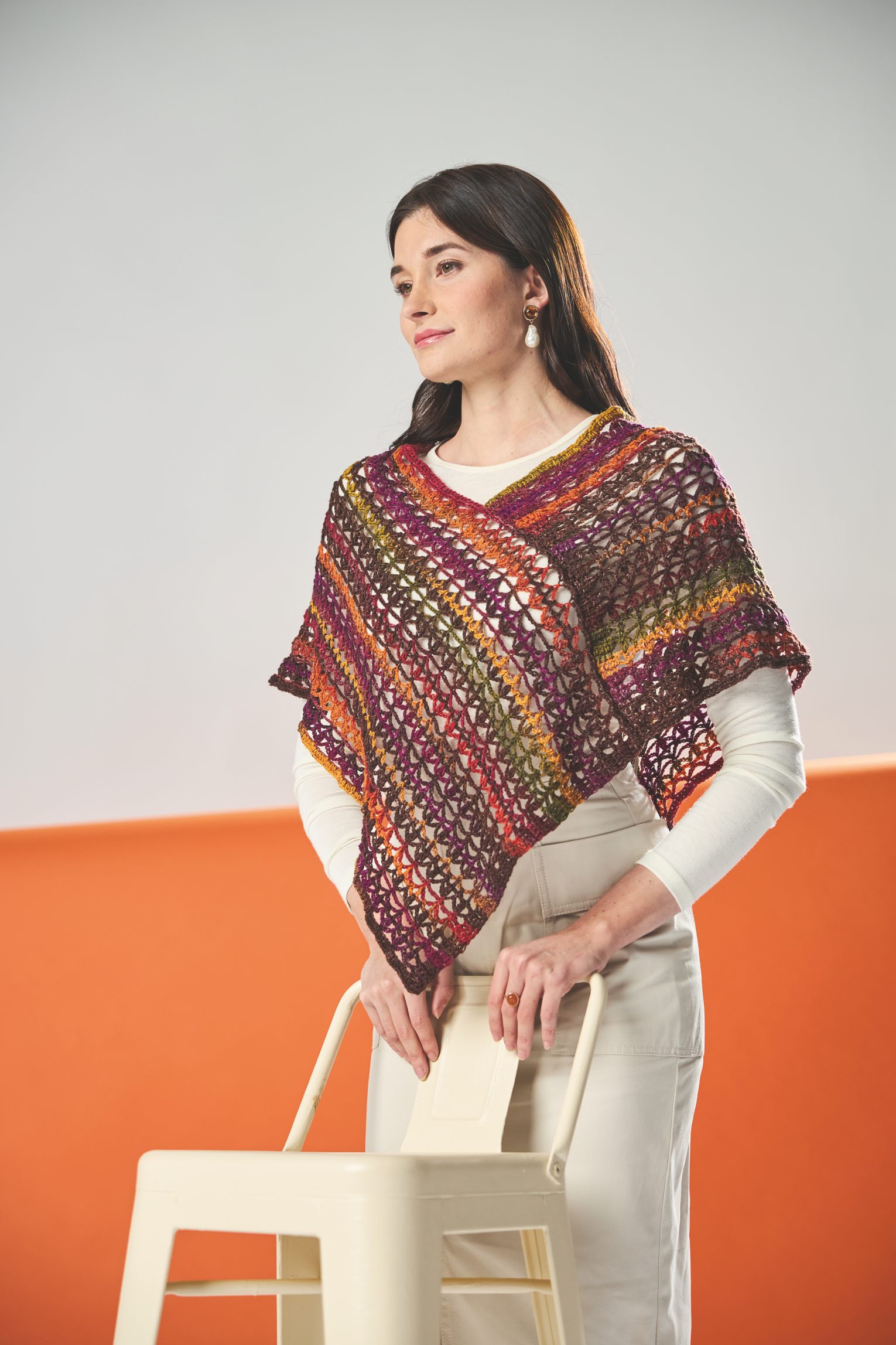 Bunter, handgemachter Poncho aus gehäkeltem Garn mit offenen Maschen, über weißer, moderner Kleidung.