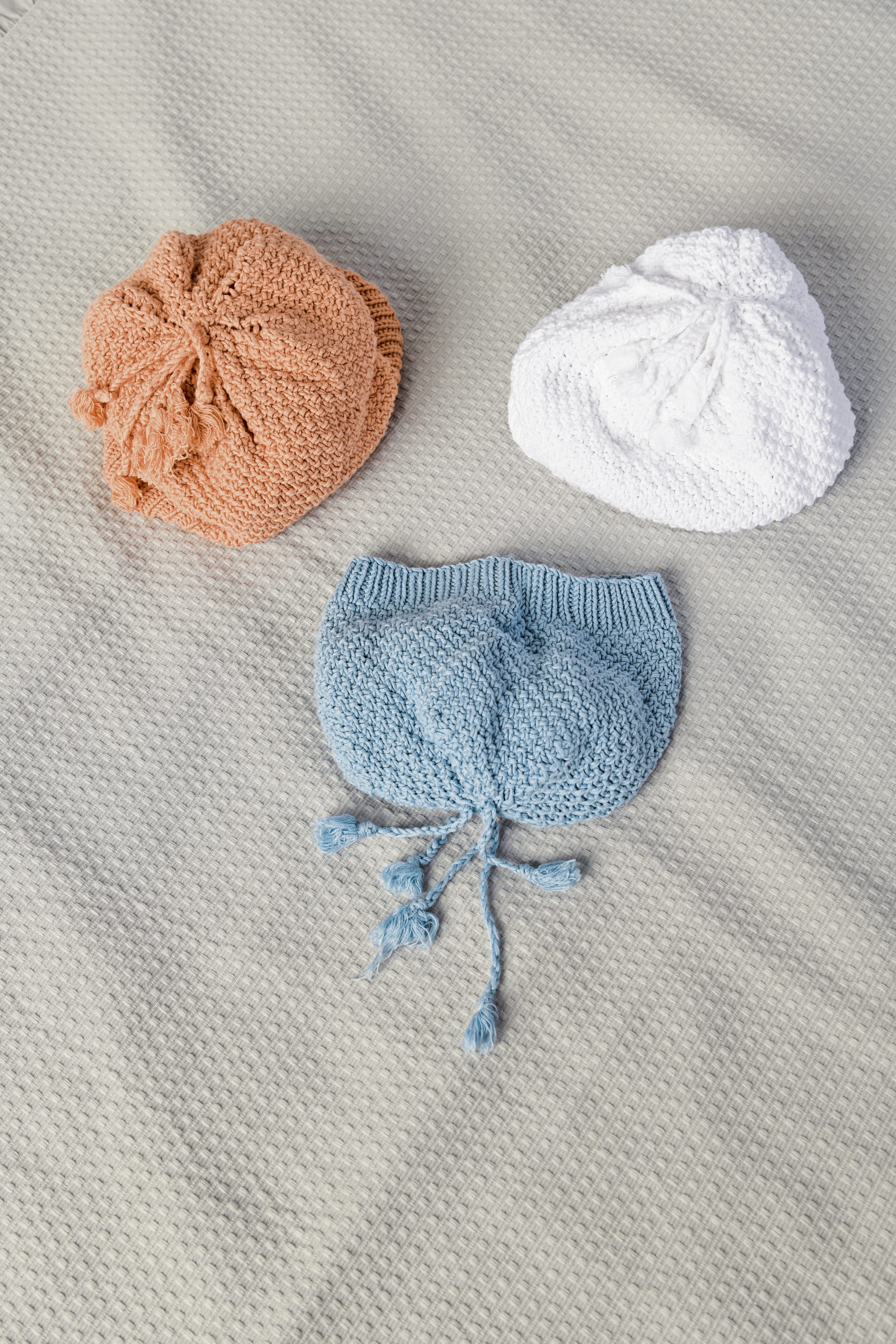 Drei handgestrickte Mützen: orange, weiß und blau; mit Kordeln. Modisch, DIY-Style.