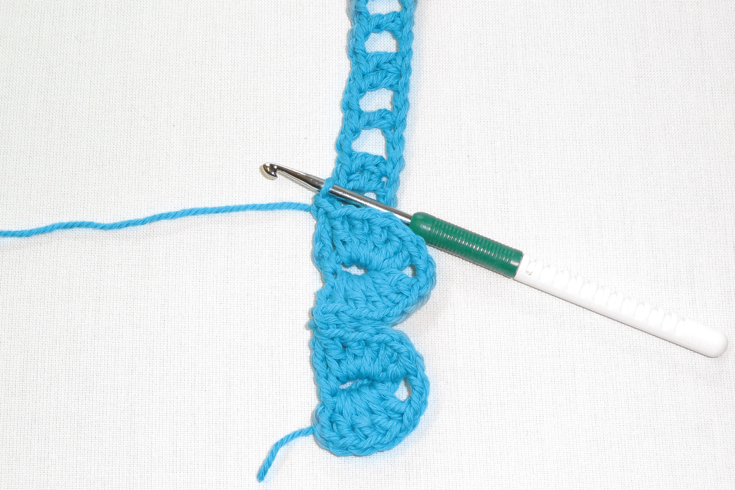 Blaues, handgemachtes Häkelstück mit Lochmuster. DIY-Kunstwerk mit bunter Häkelnadel in Aktion.