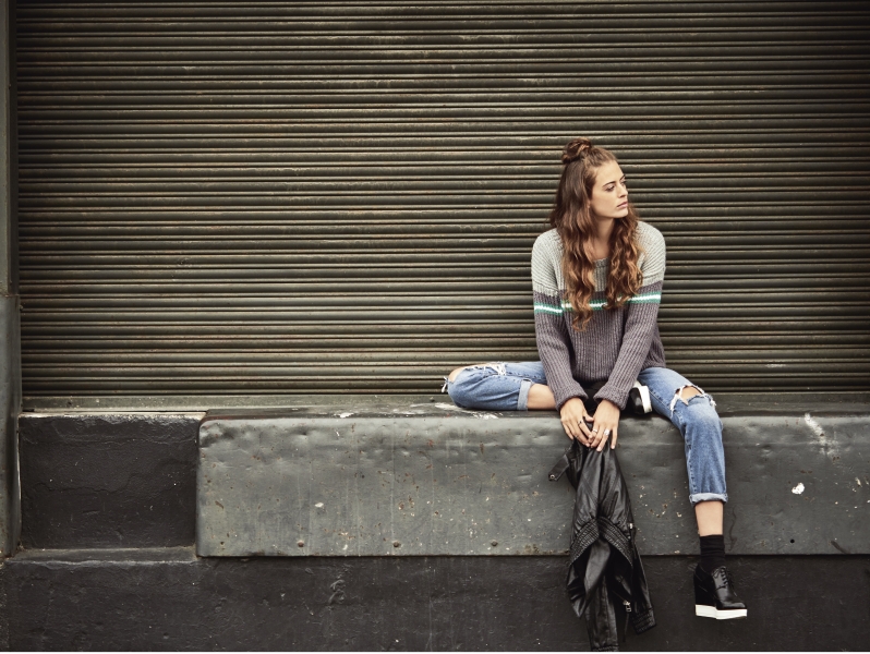 Grauer Strickpullover mit Streifen, zerrissene Jeans, schwarzes Leder lässig kombiniert, urban und modisch.