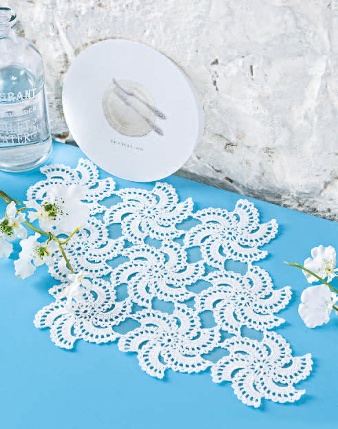 Weißes, handgehäkeltes Tischset mit filigranem, geschwungenem Muster auf blauem Untergrund. Elegant, modisch.