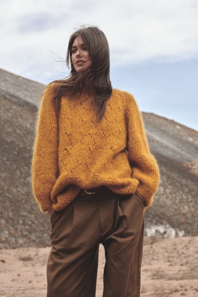 Senfgelber, grob gestrickter Pullover, weit geschnitten; kombiniert mit braunen, lässigen Hosen, handgemacht.