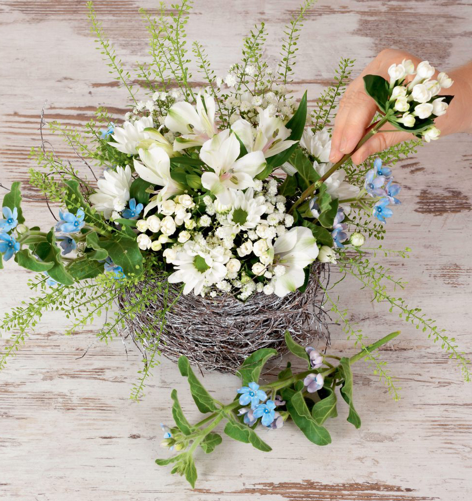 Handgemachter Blumenstrauß mit weißen Blüten, blauen Akzenten; rustikalem Drahtkorb, DIY-Charme.