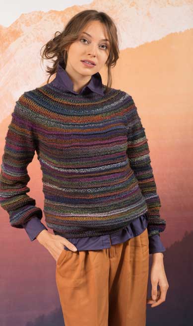 Modischer, handgemachter Pullover mit buntem Streifenmuster, kombiniert mit lila Hemd und lockeren braunen Hosen.