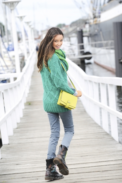 Modischer Look: grüner Strickpullover, passender Schal, gelbe Umhängetasche, Jeans und coole Stiefel.