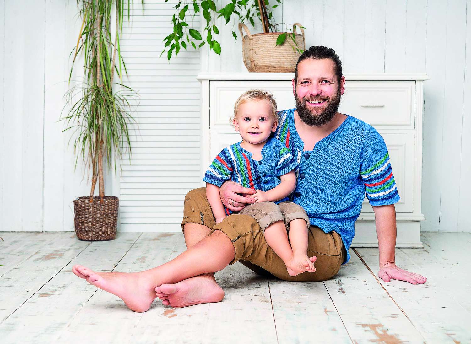 Vater und Kind in selbstgemachten, blauen Strickjacken mit bunten Streifen. Lässiger und bequemer Schnitt.
