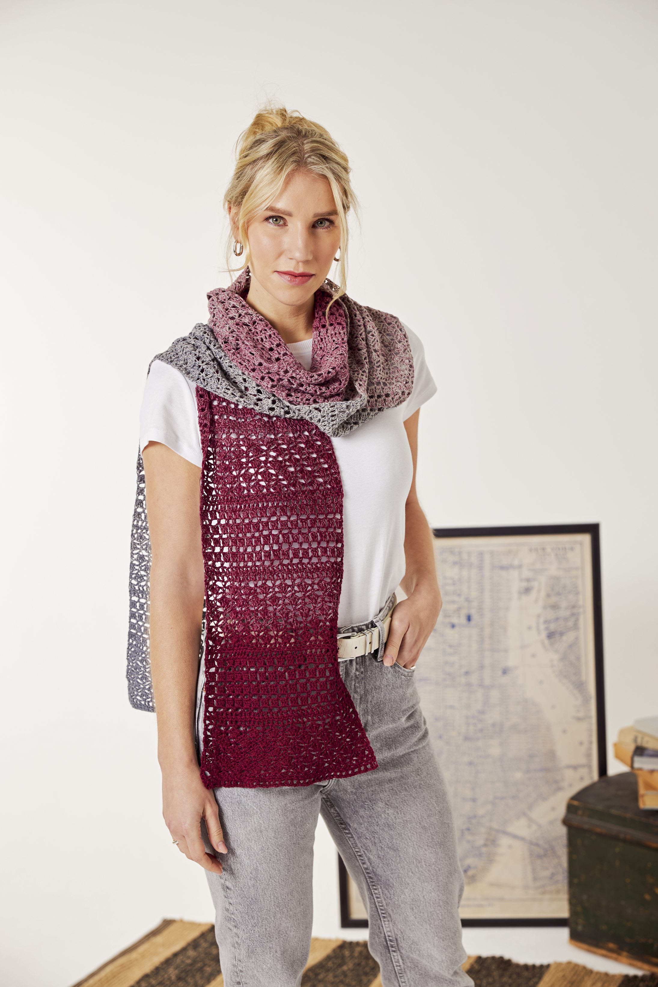 Handgemachter Schal in Grau-Rot mit gehäkeltem Muster, kombiniert mit weißem Shirt und grauer Jeans.