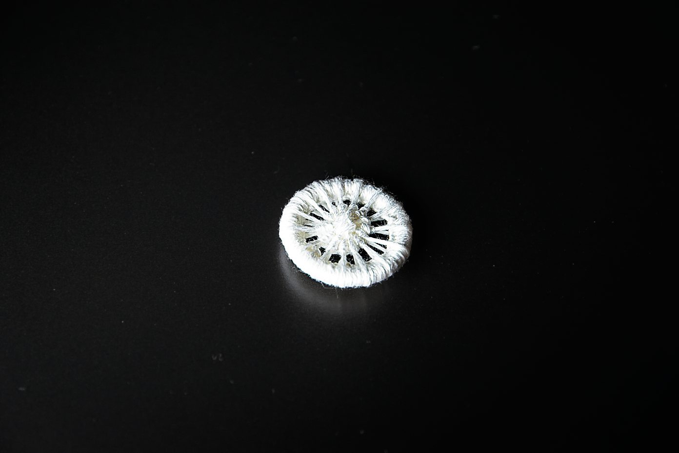 Runder, weißer Knopf, handgewebt, rautenförmiges Muster. Minimalistisch, DIY, kunstvoll.