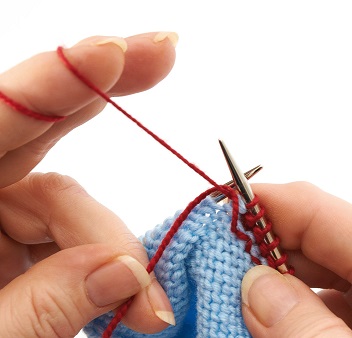 Handarbeit mit rotem Garn und blauem Strickstück. Modisches, selbstgemachtes DIY-Muster entsteht.