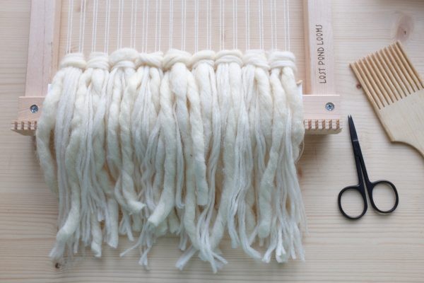 Cremefarbene, handgewebte Wolle auf einem Webrahmen, DIY, handgemacht. Naturtöne, weiche Struktur.