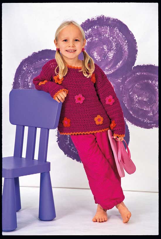Handgemachter Pullover in Lila, verziert mit Blumenmuster. Kombiniert mit leuchtend pinker Hose. Farbfroh und modern.