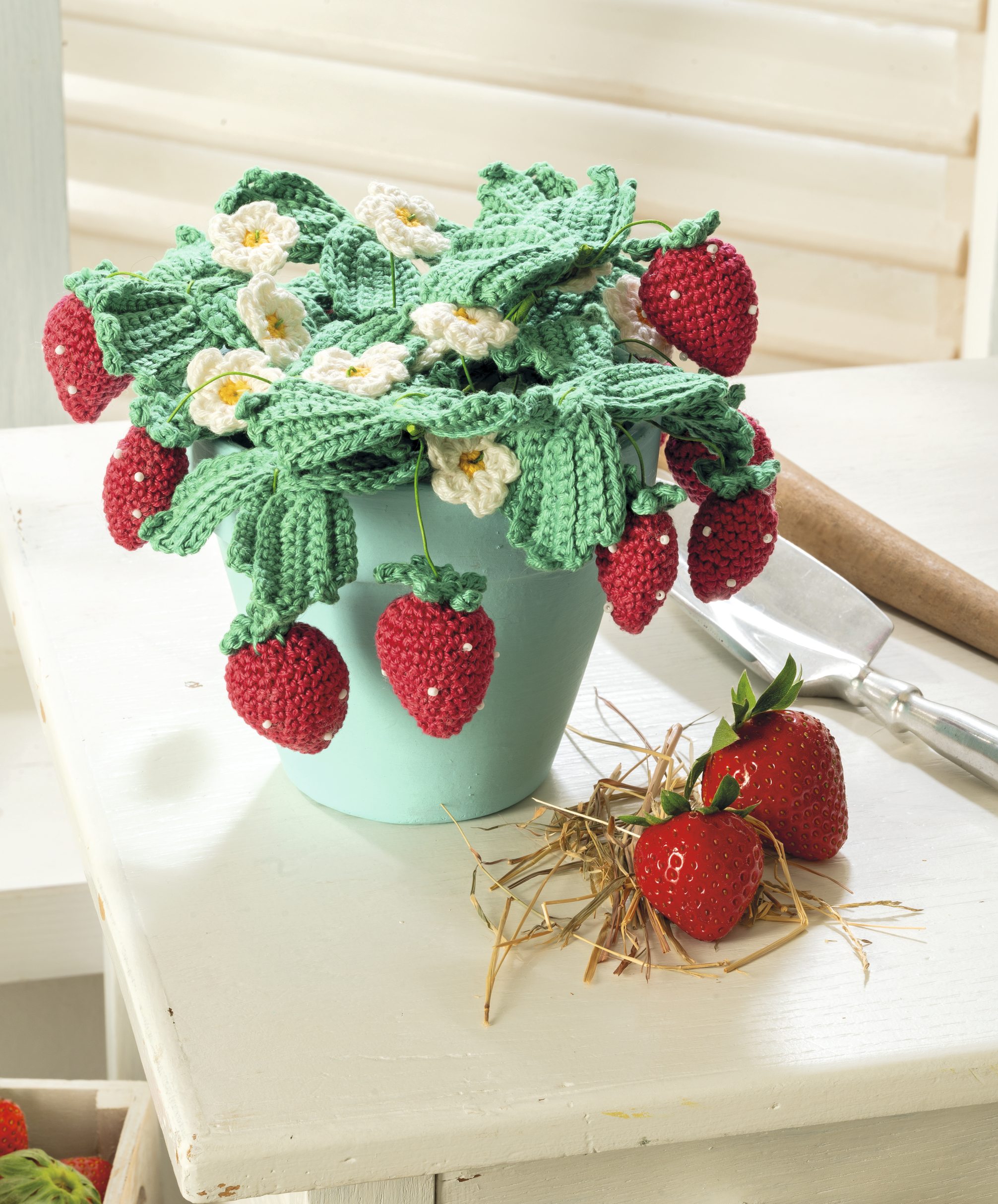 Handgemachte gestrickte Erdbeeren, Blätter und Blüten in Grün und Rot, kunstvoll und fantasievoll gestaltet.