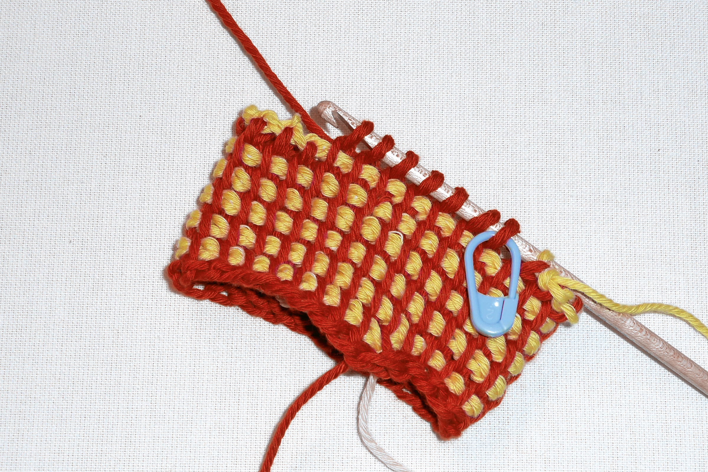 Handgemachtes Strickstück mit rotem und gelbem Muster, kreatives DIY-Projekt mit Häkelakzent.