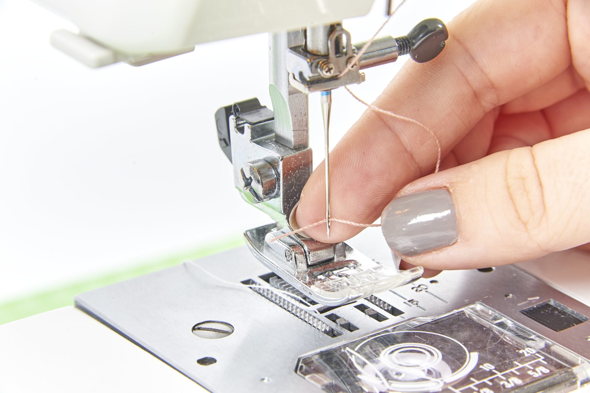 Handarbeit: Finger führen Faden in Nähmaschine ein. DIY, modisch, kreativ.