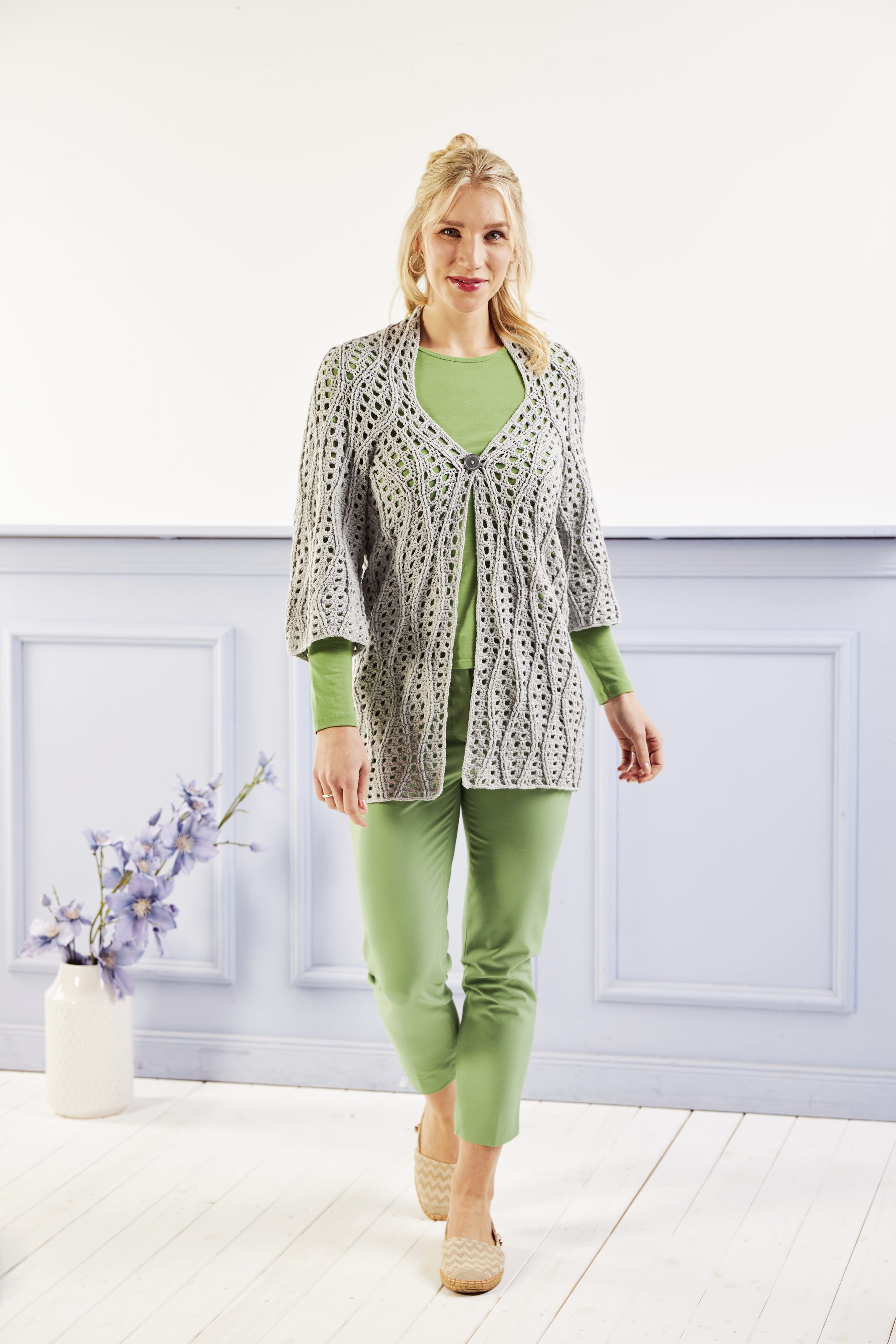 Graue gehäkelte Jacke mit elegantem Muster über grüner Kleidung. Modisch, handgemacht, stilvolle Kombination.