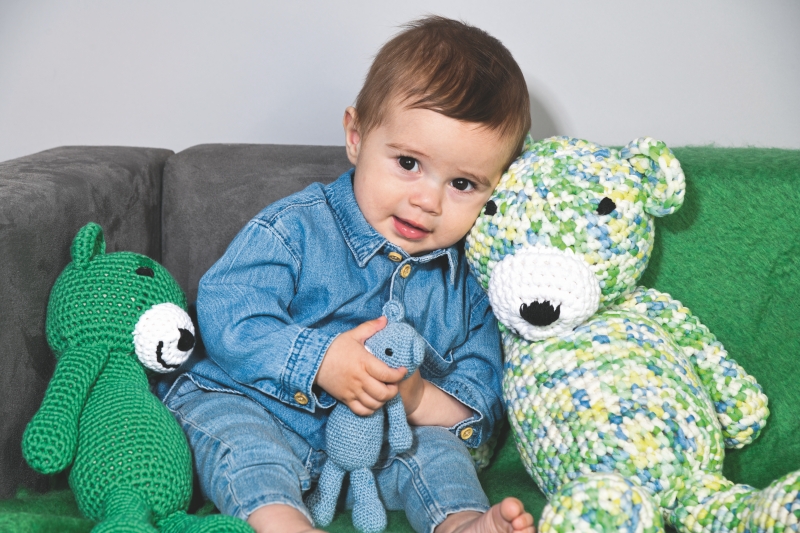 Baby in modischem Jeans-Outfit mit selbstgemachten, bunten Häkelbären: grün, blau, handgearbeitet.