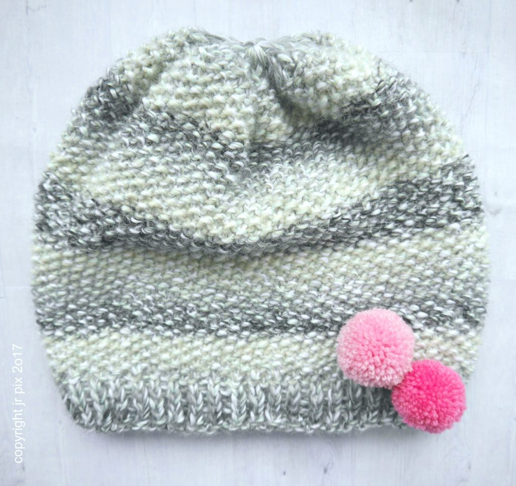 Graue handgestrickte Mütze, meliert, mit zwei rosa Pompons. Modisch, do-it-yourself, einzigartig.