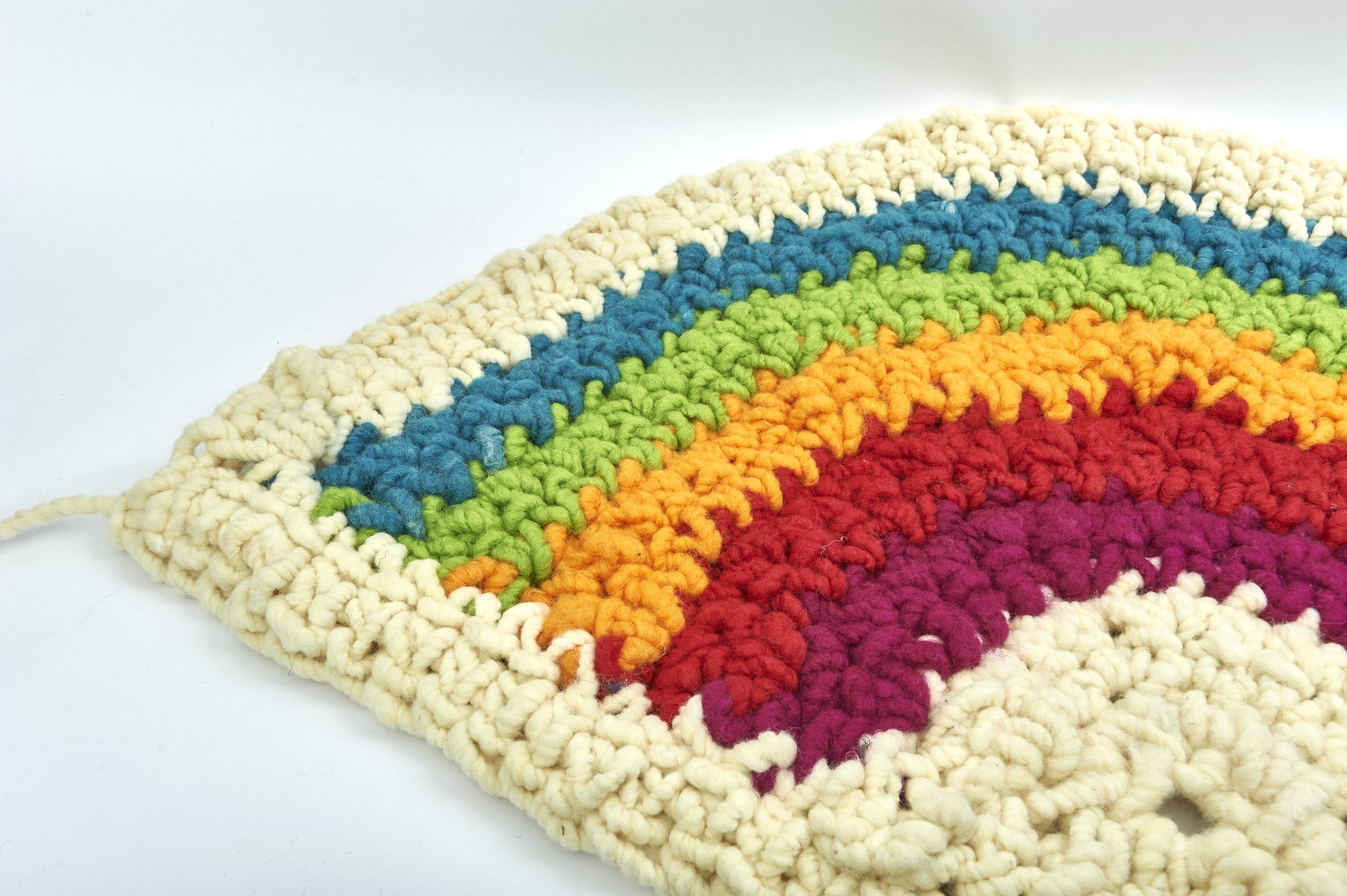 Handgemachte, bunte Häkelarbeit; kräftige Regenbogenstreifen, grobe Maschen, DIY-Stil.