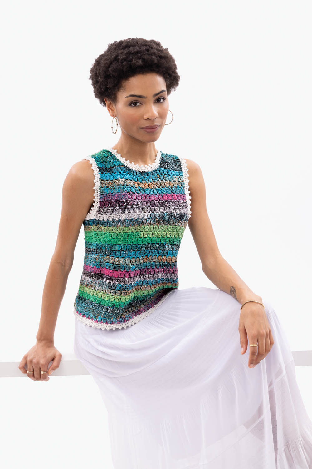 Modisches, handgehäkeltes Top mit farbenfrohen Streifen, kombiniert mit schlichtem, weißen Rock. DIY-Chic.