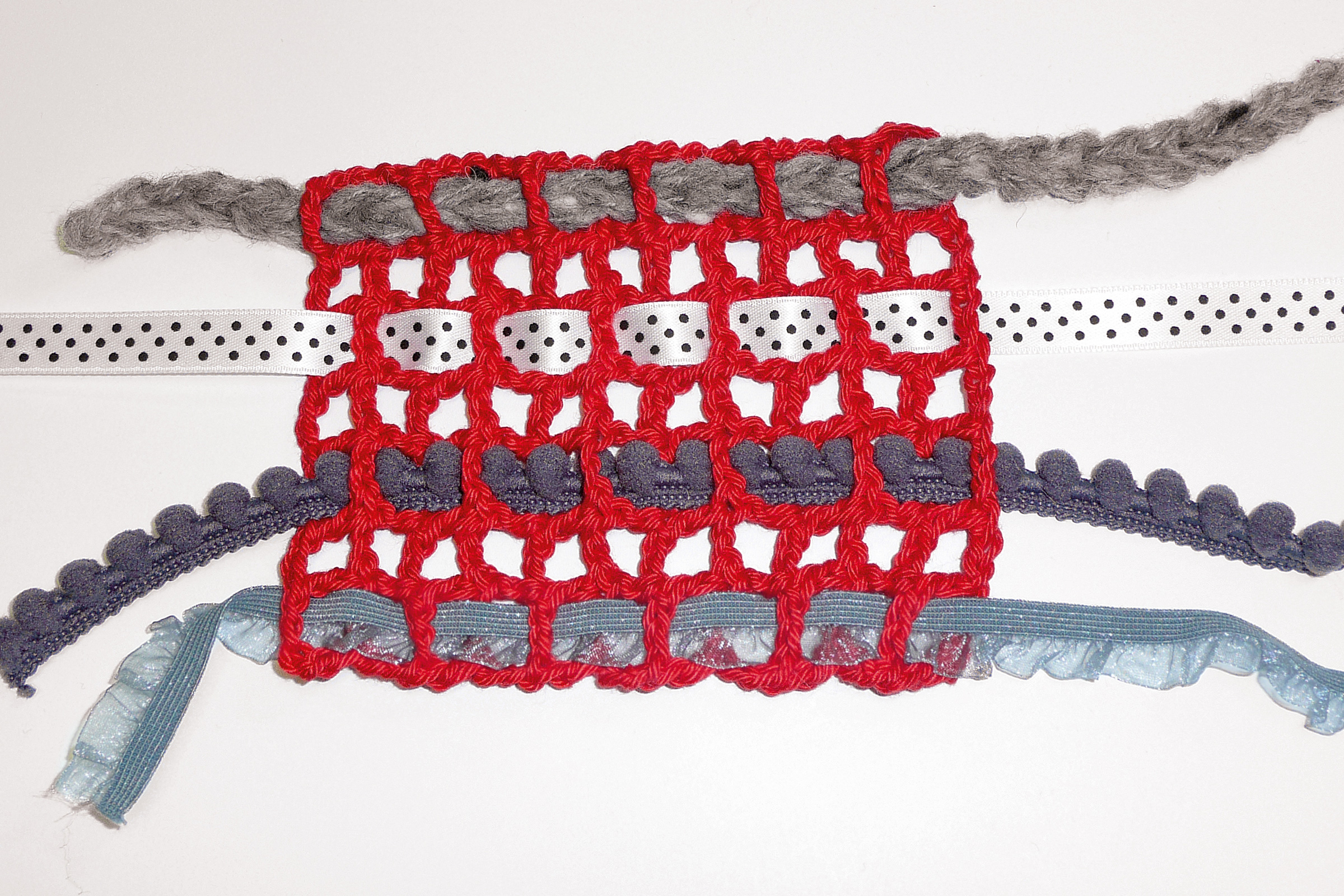 Handgefertigt, rotes Häkelgitter mit grauen und blauen Akzenten. Modisches Musterdetail.
