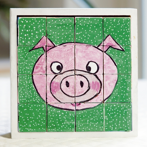 DIY Schweinmotiv auf grünem Hintergrund. Rosa Gesicht, weiß gepunktet, auf 12 quadratische Holzplatten gemalt.