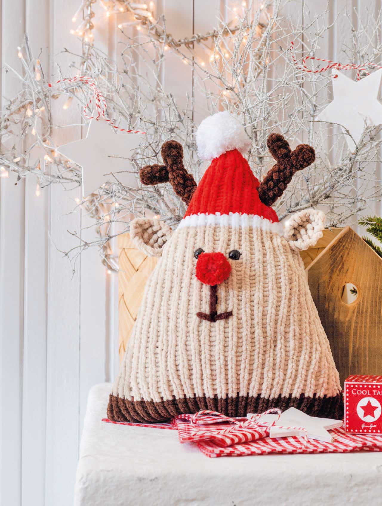 Handgemachtes Rentierkissen, rot-weiße Mütze, Plüschkugel, grobes Strickmuster, liebevoll DIY.