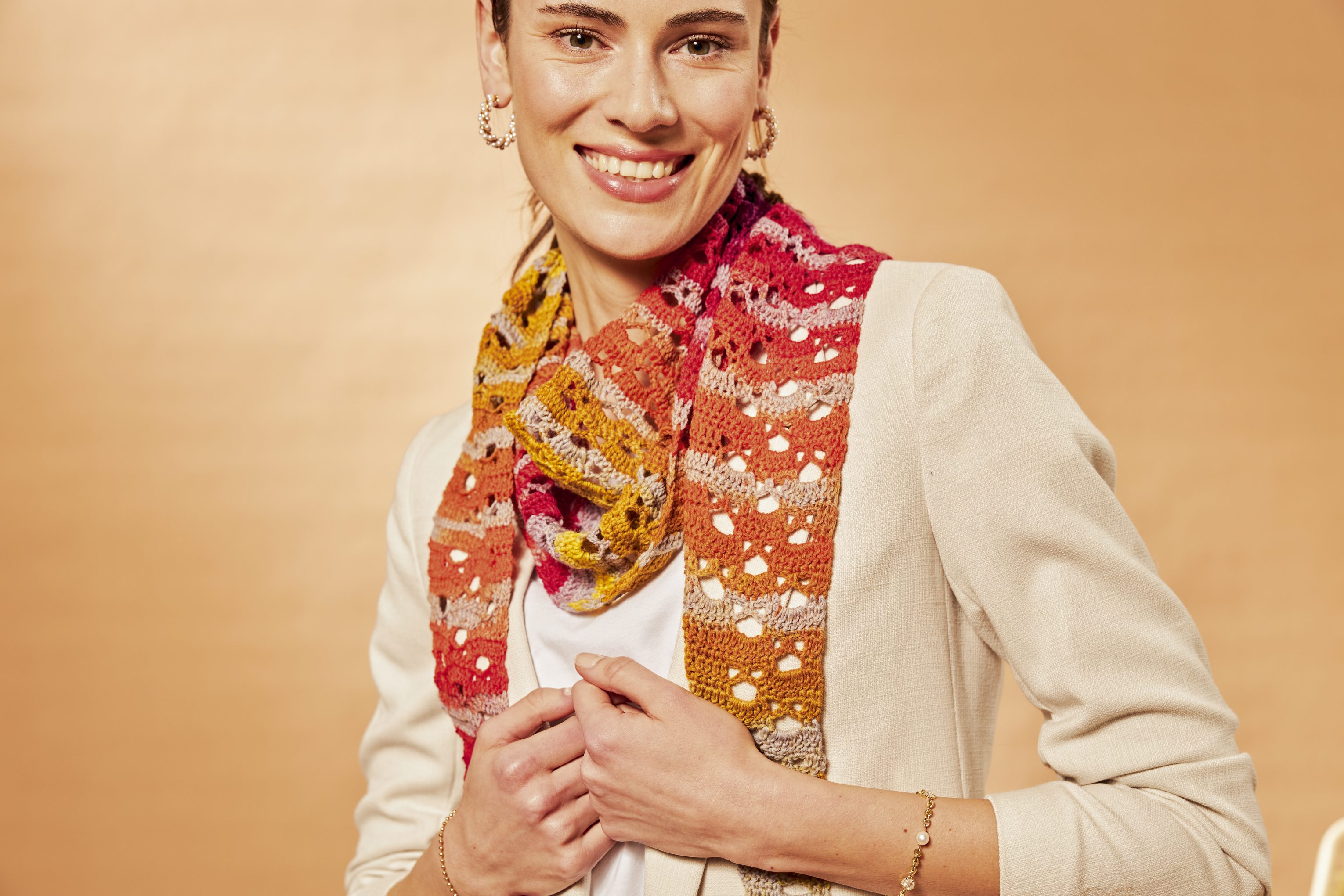 Bunter, handgemachter Häkel-Schal mit Lochmuster auf weißem Top und hellem Blazer.