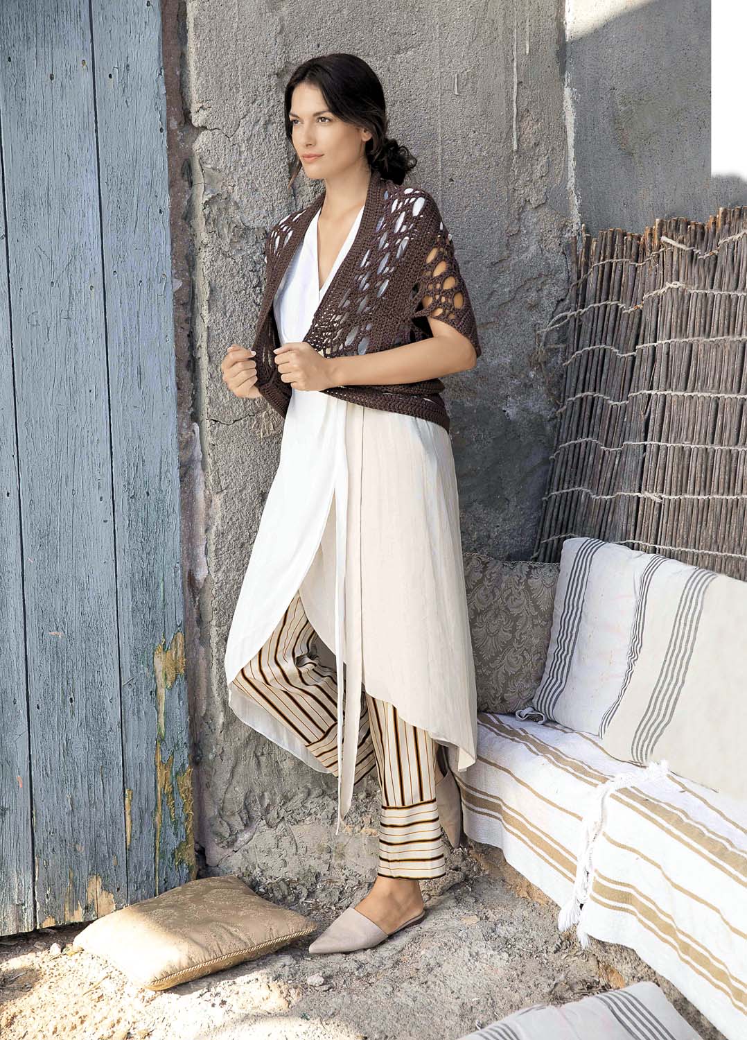Handgemachtes braunes Lochmuster-Cape, weißes asymmetrisches Kleid, gestreifte Hose; modisch & lässig.