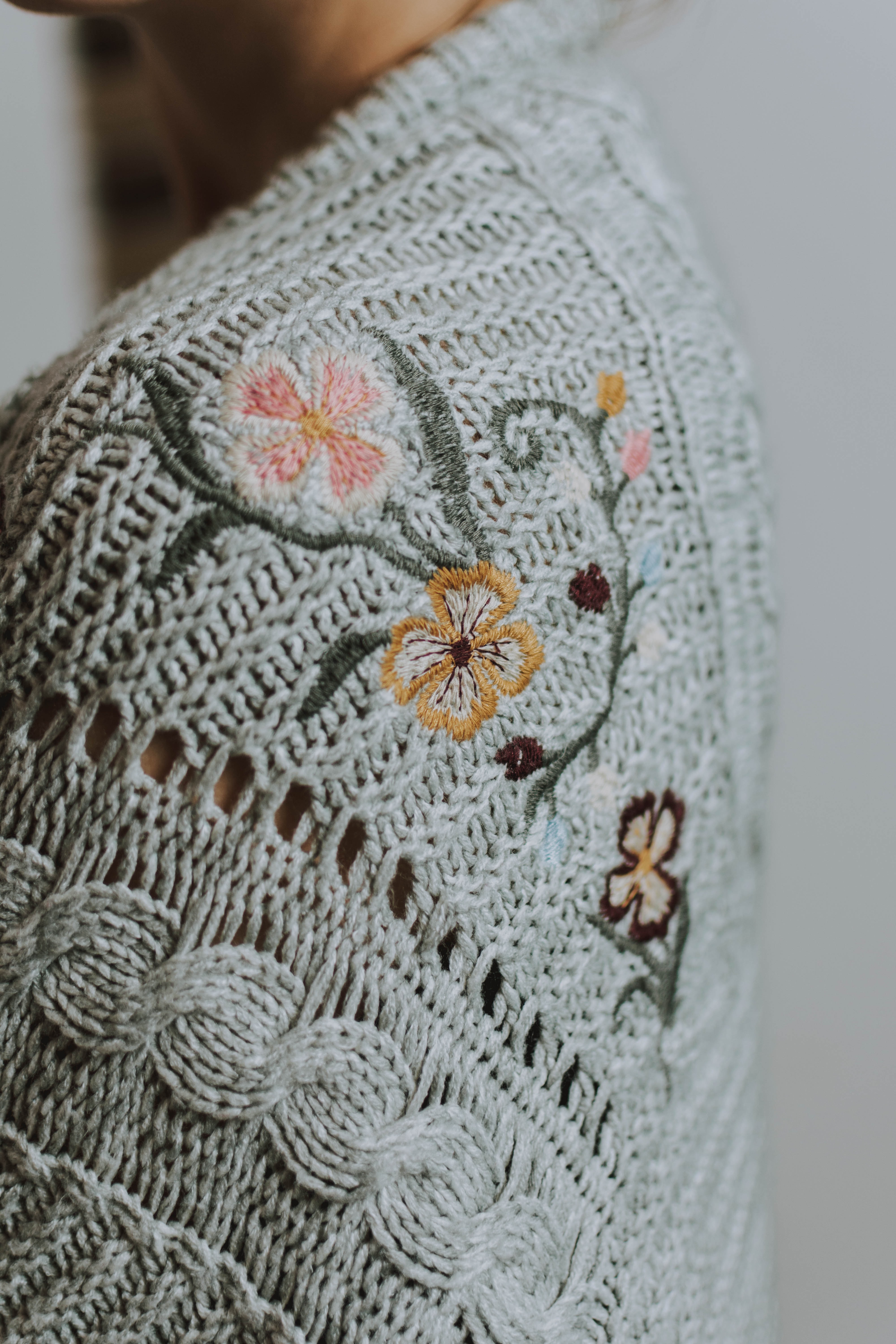 Grau gestrickte Textur mit Blumenstickerei; handgemacht, modisch, DIY, einzigartiges Muster.