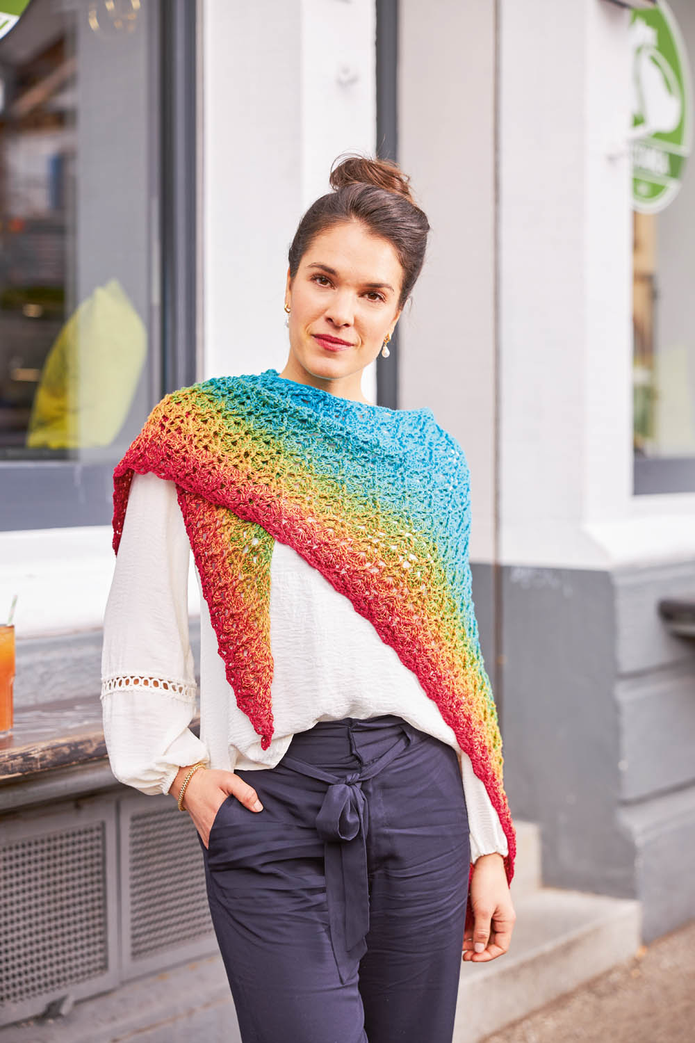 Bunter, handgemachter Schal in Regenbogenfarben, elegant über weißer Bluse drapiert. Stilvoll und einzigartig.