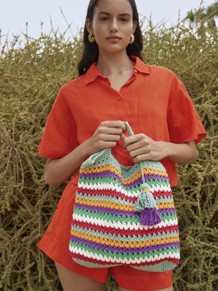 Farbige, handgemachte Tasche im Streifenmuster vor modischem, roten Leinen-Outfit.
