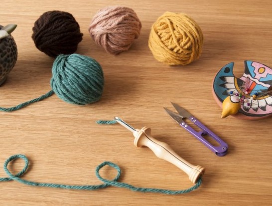 Bunte Garnknäuel in Braun, Rosa, Gelb, Türkis. DIY-Werkzeuge: Holzgriff, Schere, Nadeln. Kreative Handarbeit.
