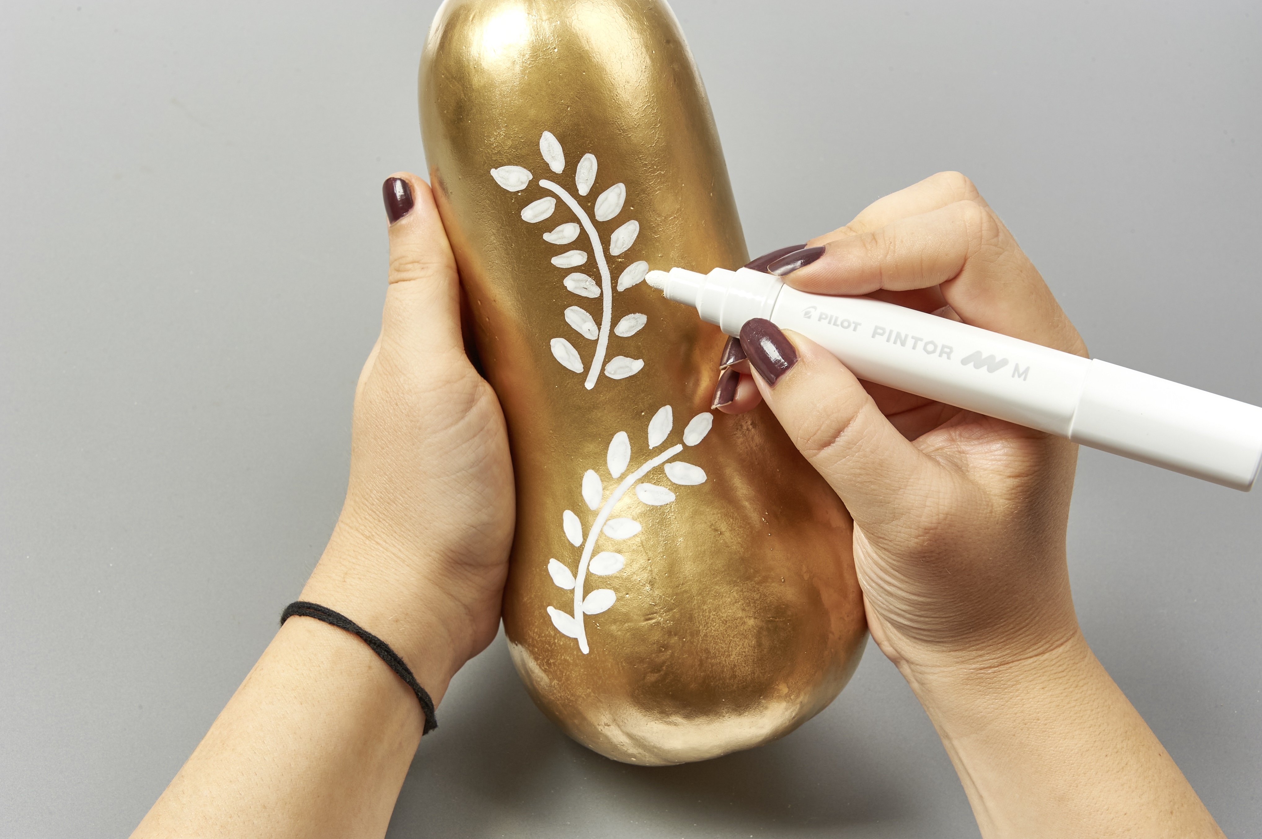 Goldene Kürbisform mit handgemaltem, weißem Blattmuster, DIY-Stil, modische Verzierung.